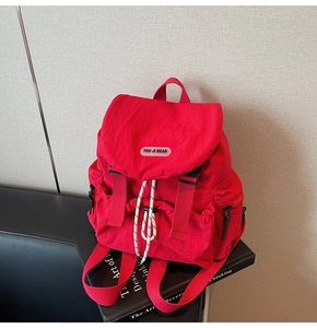 Detail of red nylon backpack with flap buckle and drawstring closure on a black book
