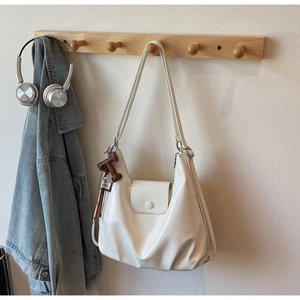 Detail of white glossy leather bucket bag with T-shaped charm hanging on a wooden hook