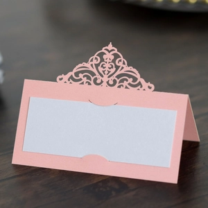 Detail of pink laser-cut place card with elegant hollow lace pattern on wood table