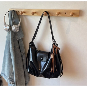Detail of glossy black patent leather shoulder bag featuring a brown brand charm and flap closure