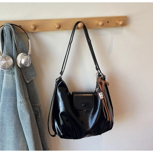 Detail of glossy black leather tote bag with brown horse pendant on wooden rack