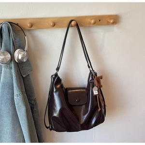 Detail shot of a glossy dark brown leather shoulder bag with decorative charms and metal clasp