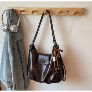 Deep brown glossy PU leather hobo bag with a T-letter pendant hanging on a wooden hook