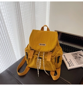 Detail of mustard yellow nylon backpack featuring top flap and double buckle straps