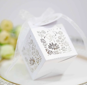 Macro shot of white laser-cut hollow daisy patterns on a cube gift box with ribbon
