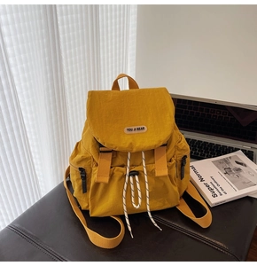 Detail of yellow nylon backpack featuring flap buckle and drawstring closure on a desk