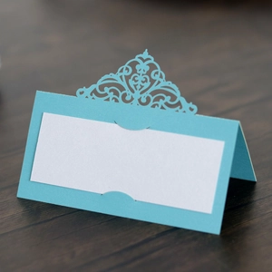 Detail view of light blue laser-cut place card with ornate hollow floral patterns on wood