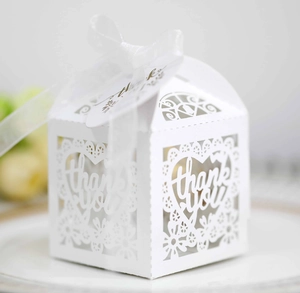 Close-up of white laser-cut wedding favor box with lace heart and thank you ribbon