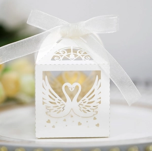 Close-up of white laser-cut wedding favor box featuring swan heart design and organza ribbon