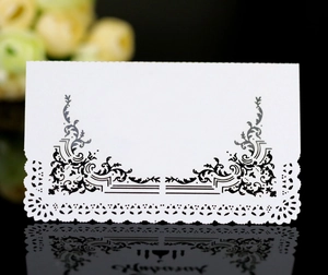 Close-up of white lace place card with black baroque scrolls and laser-cut edges