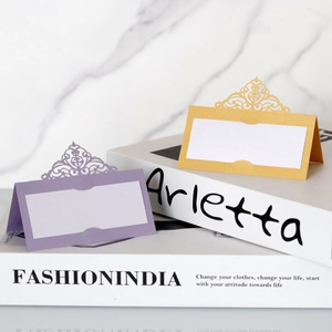 Close-up of laser-cut crown place cards in purple and gold on marble background