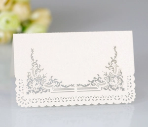 Detailed view of white pearl paper place card with hollow lace cut and silver scroll pattern