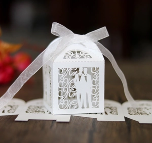 Macro detail of white laser-cut 'Mr & Mr' wedding favor box with elegant organza ribbon