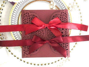 Laser cut burgundy wedding invitation card with elegant satin ribbons on ceramic plate