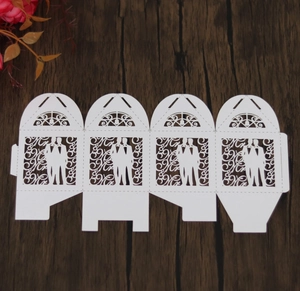 Flat lay of laser-cut white wedding candy boxes with intricate silhouettes of two grooms