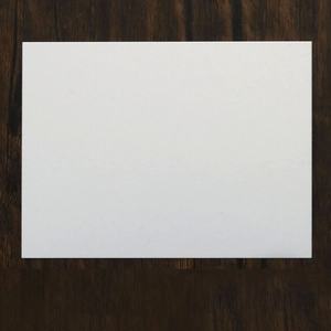 Detailed view of blank white pearlescent paper invitation card on dark wood background