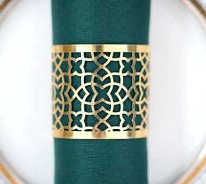 Close-up of golden geometric hollow metal napkin ring on dark green fabric napkin
