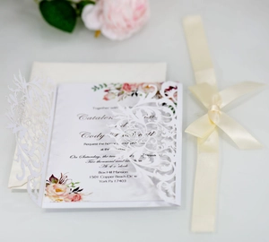 Close-up of laser-cut floral wedding invitation with cream satin ribbon and white envelope
