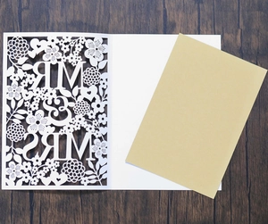 Macro view of laser-cut floral wedding invitation sleeve with Mr & Mrs on wood background