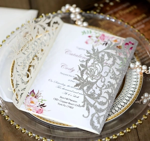 Detail of laser-cut wedding invitation with silver glitter finish and floral inner card