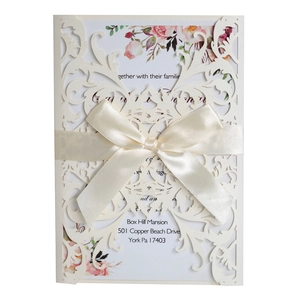 Detail of laser-cut floral invitation with cream satin ribbon and pink rose inner page
