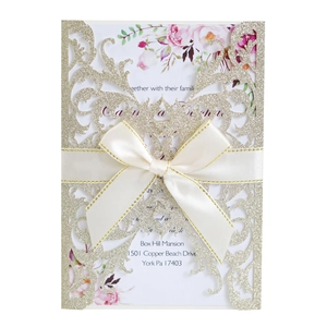 Detail of laser-cut rose invitation card with gold glitter pattern and white satin bow