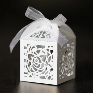 White laser-cut rose candy gift box with elegant organza ribbon on dark wood surface