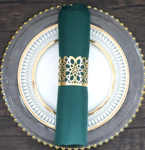 Detail of laser-cut gold metal napkin ring with hollow floral pattern on a green napkin