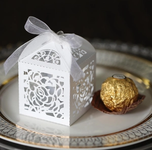 Detailed laser-cut rose hollow candy box with a white ribbon bow on a ceramic plate