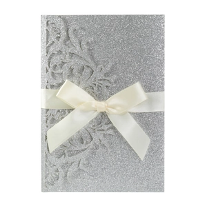 Detail of silver glitter wedding invitation with laser-cut floral design and satin bow