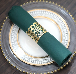 Detail of laser-cut golden floral napkin ring on dark green cloth and white gold plate