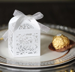 Close-up of laser-cut white rose favor box with silver bow on an elegant porcelain plate