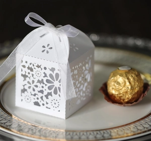 Detailed laser cut white floral candy box with a ribbon on a gold-rimmed plate