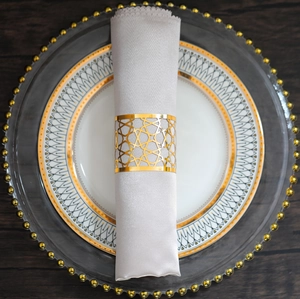 Detail of a golden geometric star napkin ring with luxury silver satin napkin on dinnerware