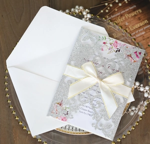 Dettaglio invito matrimonio glitter intagliato a laser con carta floreale e fiocco avorio