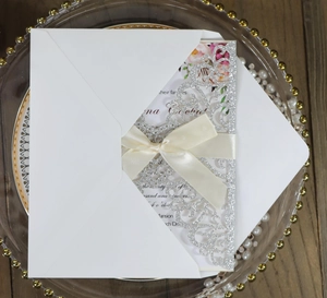 Detail of glitter laser-cut wedding invitation with white ribbon bow and floral card