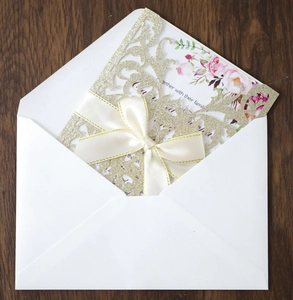 Detail of laser-cut rose invitation with glitter cover, ribbon bow and white envelope
