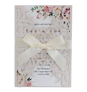 Close-up of laser-cut floral wedding invitation with cream ribbon bow and rose patterns