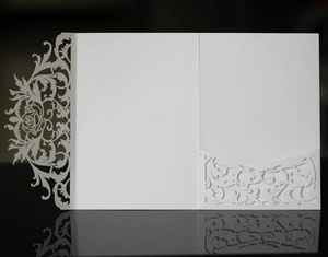 Macro shot of laser-cut white pearlescent paper invitation with intricate floral hollow design