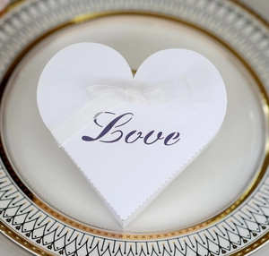 Close-up of white heart-shaped candy box with laser-cut LOVE text and organza ribbon