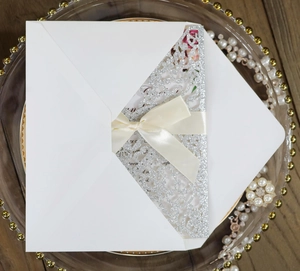 Close-up of laser-cut glitter silver wedding invitation with silk ribbon and envelope