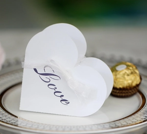 Detail of white heart-shaped gift box with purple Love text and white ribbon on a gold plate