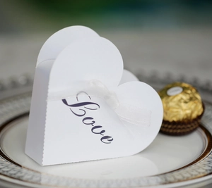 Close-up of heart-shaped gift box with Love script, white ribbon and chocolate detail