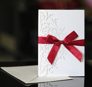 Detail of laser-cut floral wedding invitation with a decorative red satin ribbon bow