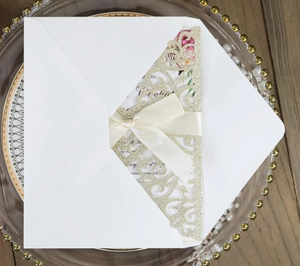 Detail of laser cut champagne glitter wedding invitation with beige silk ribbon and envelope