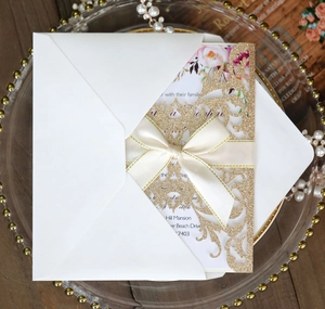 Detailed laser-cut gold glitter wedding invitation with elegant beige satin ribbon bow