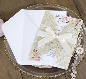 Detail of laser-cut glitter wedding invitation with champagne gold floral sleeve and bow