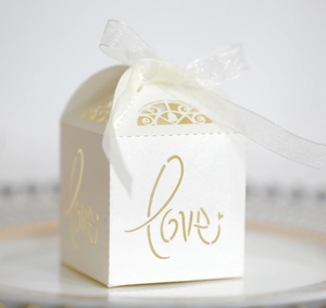 Macro shot of white laser-cut wedding candy box with gold LOVE text and ribbon bow