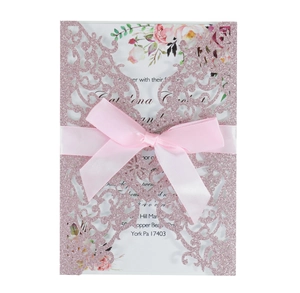 Detail of pink glitter laser cut wedding invitation with ribbon and floral insert