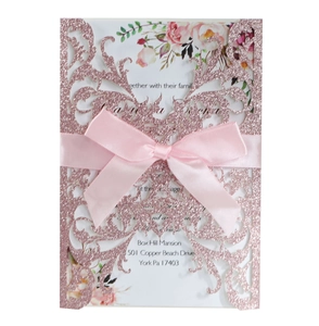 Close-up of laser-cut rose wedding invitation with pink glitter finish and satin bow